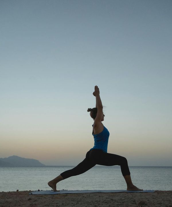 Woman greeting the sunrise with an energetic yoga pose, silhouette against warm sky.